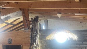 A wooden interior with a sloped ceiling, a bed with a floral bedspread, a ceiling fan, and a wall-mounted light fixture. - Enjoyable 1-bedroom chalet with AC in charming Hamallaj (Hamallaj)