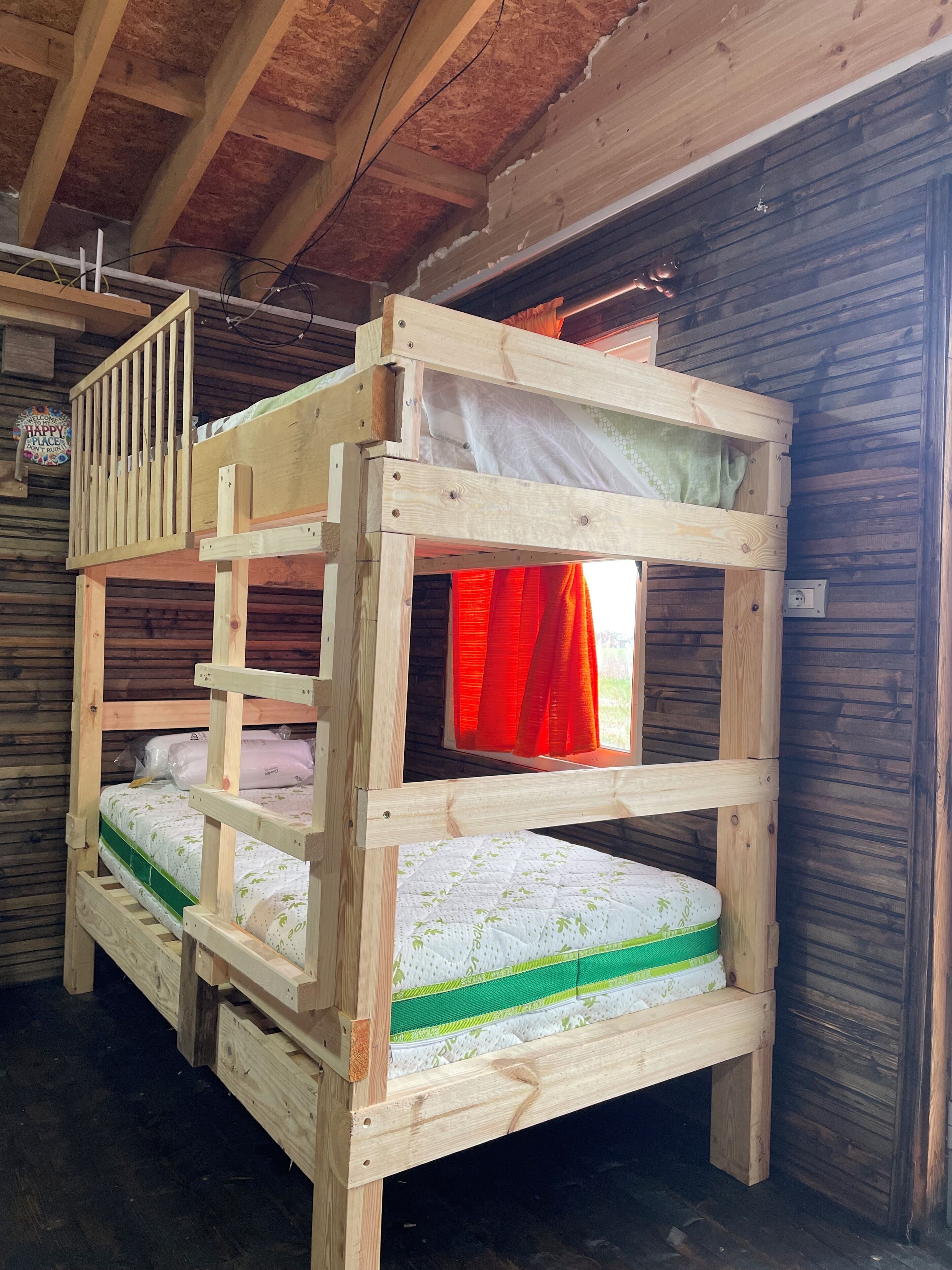Un lit superposé avec une échelle, une fenêtre avec des rideaux rouges et un mur en bois.
