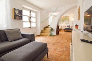 A modern living room with a grey sofa, a staircase leading to another room, and a TV on a white stand. - La Calma deVilo (Vilo)