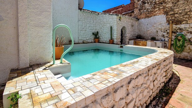 Une piscine dont le fond et les bords sont recouverts de carreaux de pierre, agrémentée de plantes en pot et bordée d’un mur en pierre.