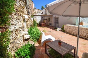A stone-walled courtyard with a wooden table, white plastic chairs, and a white umbrella providing shade. - La Calma deVilo (Vilo)