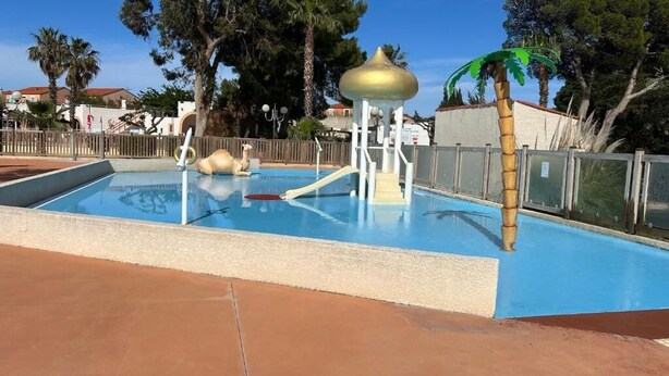 Une piscine avec un toboggan et une petite structure surmontée d’un dôme doré.
