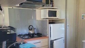 Een kleine keuken met een spoelbak, fornuis, magnetron en koelkast.
