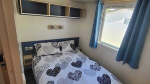 Een slaapkamer met een bed, een plank boven het bed, een raam met gordijnen en een deur.