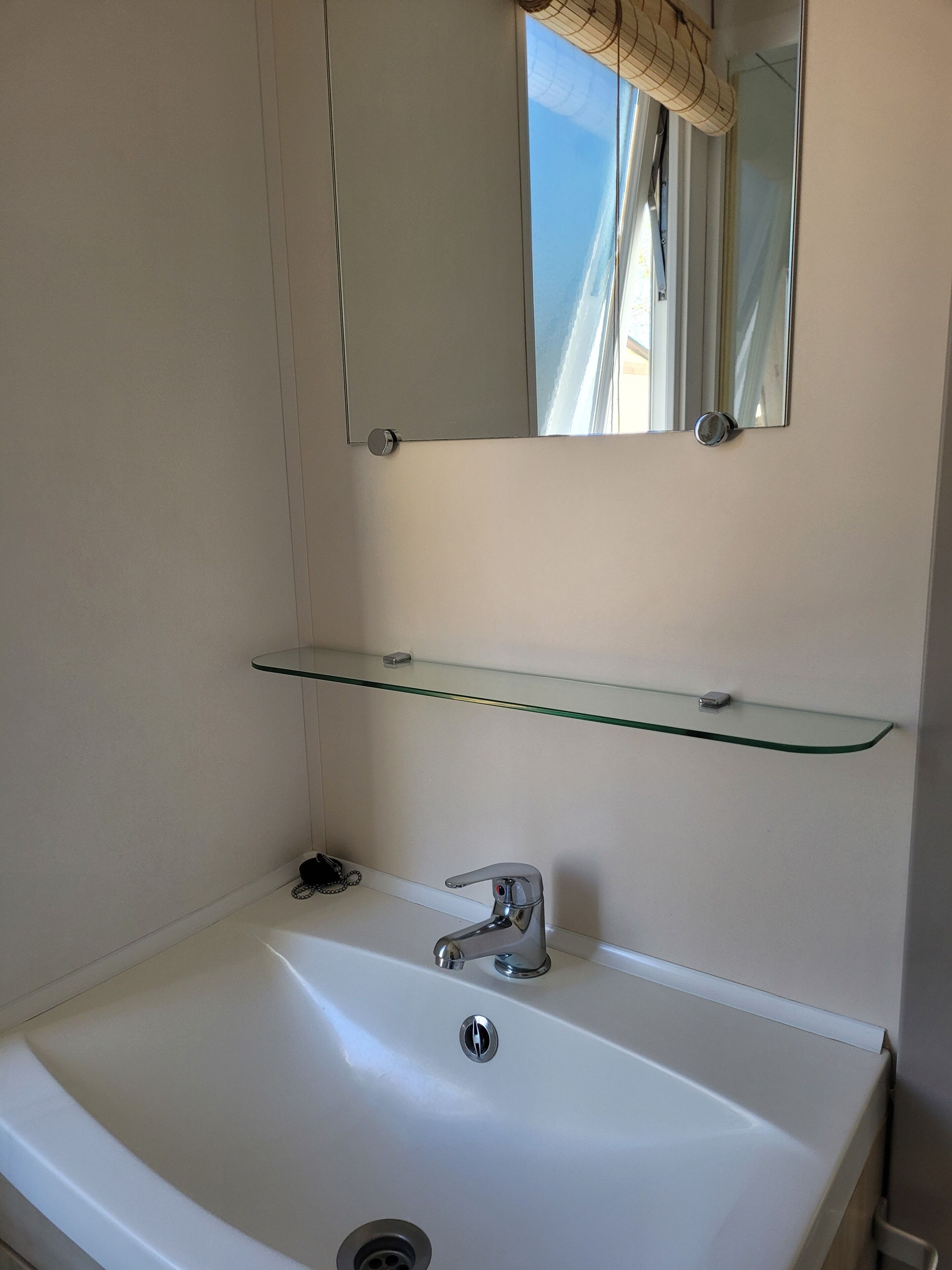 A bathroom with a white sink, a mirror above it, and a glass shelf below.