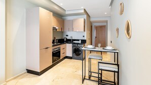 Uma cozinha compacta com eletrodomésticos modernos, uma área de refeições com um banqueta e uma máquina de lavar.