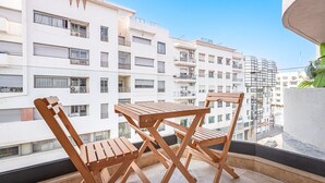 Varanda com cadeiras e mesa de madeira, com vista para uma área residencial com edifícios brancos.