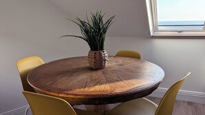 A round wooden table with a woven plant centerpiece, surrounded by yellow chairs in a room with wooden flooring and a skylight. - Cosy loft on the beach (Tramore)