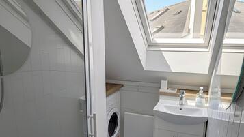 Une salle de bain moderne avec un puits de lumière, des toilettes, un lave-linge et un lavabo.