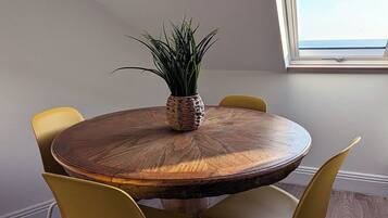 A round wooden table with a woven plant centerpiece, surrounded by yellow chairs in a room with wooden flooring and a skylight.