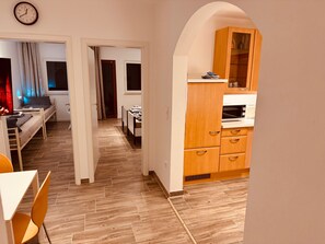 Eine moderne Wohnung mit Holzboden, einer Küche mit Holzschränken, einem Essbereich mit Tisch und Stühlen sowie einem Schlafzimmer mit Bett und Vorhängen.