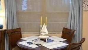 Un comedor con una mesa redonda, cuatro sillas y un ventanal con cortinas.