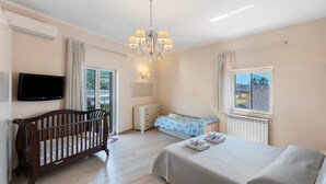 A bedroom with a crib, a bed, a dresser, a television, and a window with a view. - Apartment 'Diegopas' with Sea View, Wi-Fi and Air Conditioning (Sant'Antonio Abate)