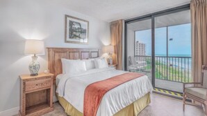 Ein Hotelzimmer mit Bett, Nachttisch, Lampe, Stuhl und einem Balkon mit Aussicht.