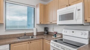 Eine Küche mit Holzausstattung, einer Mikrowelle, einem Backofen, einer Kaffeemaschine und einem Fenster mit Jalousien.
