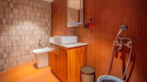 Ein Badezimmer mit Toilette, Waschbecken, Spiegel, Dusche und Mülleimer.