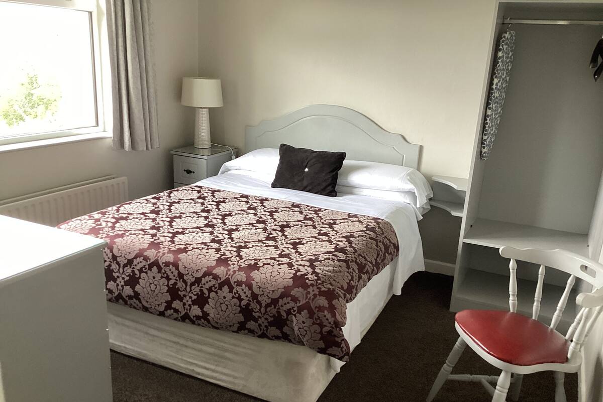 A bedroom with a bed, bedside table, lamp, chair, and a window.