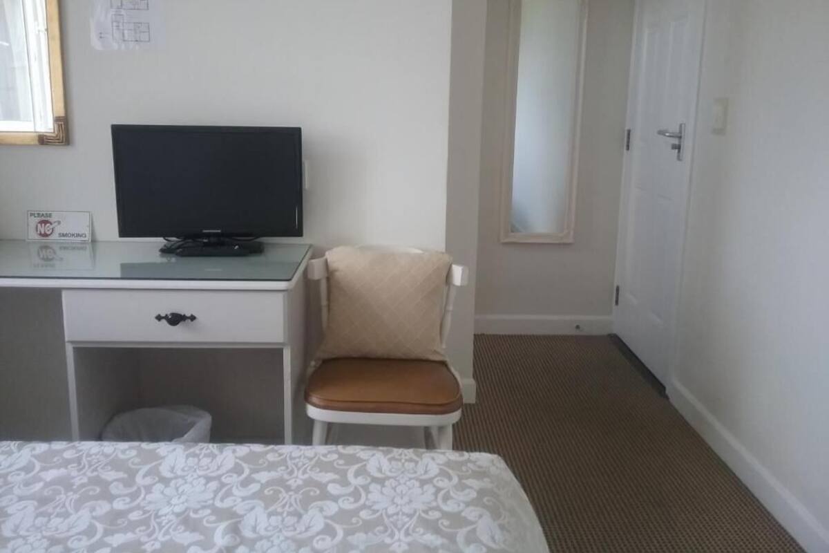 A hotel room with a bed, a desk with a television, a chair, a door, and a carpeted floor.