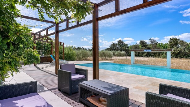 Un espace aménagé au bord de la piscine, avec des meubles en osier, un coin salon abrité et une vue sur la piscine.
