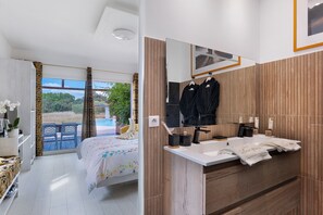 A modern bedroom with a large bed, a bathroom with a wooden vanity, and a view of the outdoors. - “Domaine des Lucques” Guest Room with Private Pool, Wi-Fi, and Air Conditioning (Mirepeisset)