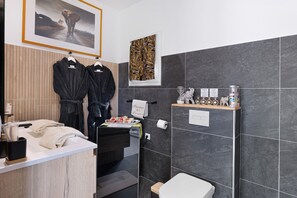 A bathroom with a shower, a toilet, a sink with a towel, and a framed picture on the wall. - “Domaine des Lucques” Guest Room with Private Pool, Wi-Fi, and Air Conditioning (Mirepeisset)