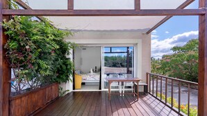 Une terrasse en bois avec une table et des chaises, une clôture en bois et une vue sur une chambre à coucher à travers une porte vitrée.