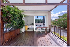 A wooden deck with a table and chairs, a wooden fence, and a view of a bedroom through a glass door. - “Domaine des Lucques” Guest Room with Private Pool, Wi-Fi, and Air Conditioning (Mirepeisset)