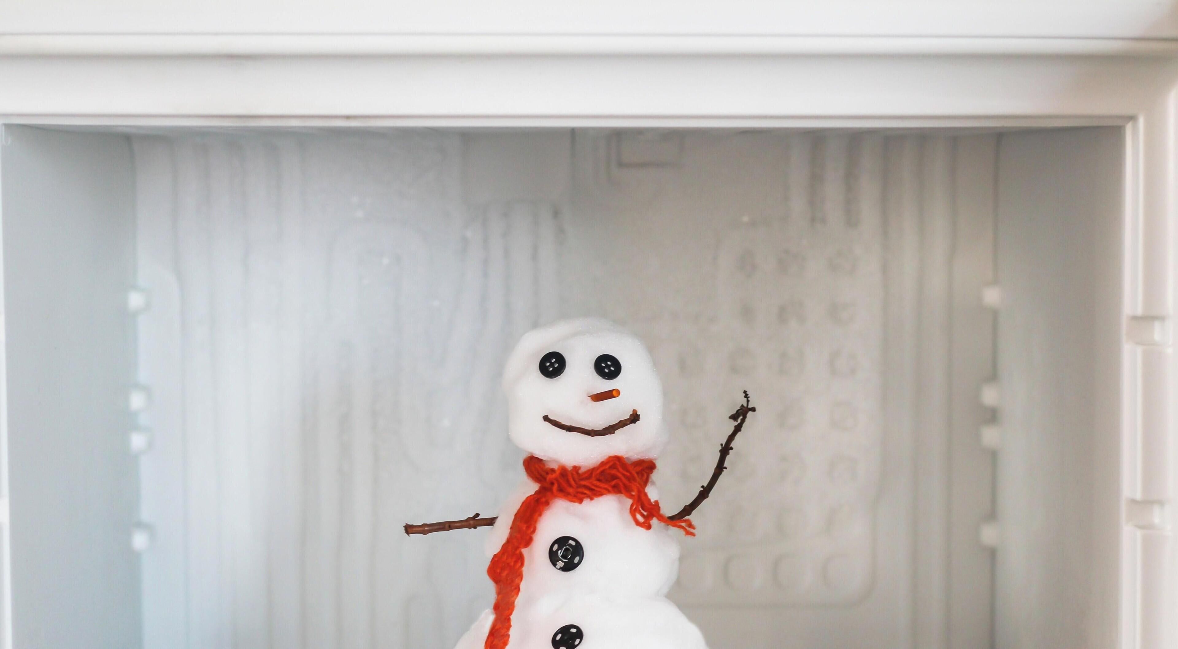 Un bonhomme de neige avec une écharpe rouge et des boutons, placé dans un four à micro-ondes.