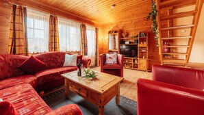 Ein Holzblockhaus-Innenraum mit Sofa, Sessel, Couchtisch, Fernseher und Regalen.