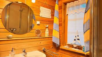 A wooden cabin bathroom with a sink, mirror, towel rack, and a window with a sailboat decoration.