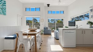 A modern kitchen with a dishwasher, a dining area with a table and chairs, and a seating area with a sofa. - The Loft- SeaMist Huskisson (Huskisson)