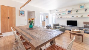 A modern living room with a wooden dining table, chairs, a sofa, and a TV. - Charming Oléron Holiday Home Near Beach with Terrace, Private Garden & Wi-Fi (Saint-Pierre-d'Oléron)