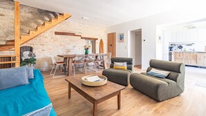 A living room with a sofa, a coffee table, and a dining area with chairs and a table. - Charming Oléron Holiday Home Near Beach with Terrace, Private Garden & Wi-Fi (Saint-Pierre-d'Oléron)