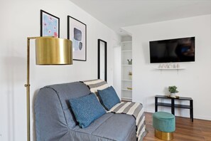 A modern living room with a sofa, a floor lamp, a television, and a small table with a plant. - Charming 2BR Retreat by République (Paris)