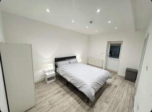 Een slaapkamer met een bed, nachtkastjes, een raam en een radiator.
