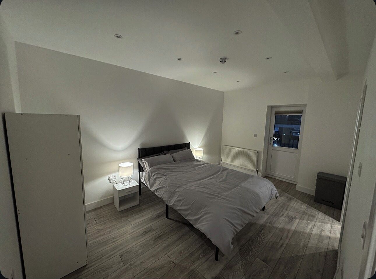 Een slaapkamer met een bed, nachtkastjes, een radiator, een raam en een deur.