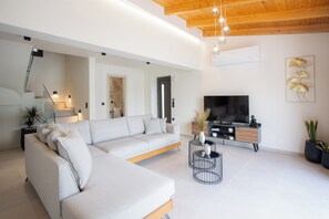 A modern living room with a sectional sofa, a TV, and a minimalist decor. - Villa Pietra di Mare-Yeni-Nidri-Lefkada (Geni)