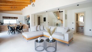 Uma sala de estar moderna com um sofá modular, uma mesa de jantar com cadeiras e duas mesas laterais redondas com vasos.