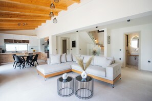 A modern living room with a sectional sofa, a dining table with chairs, and two round side tables with vases. - Villa Pietra di Mare-Yeni-Nidri-Lefkada (Geni)