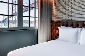 A hotel room with a large window, a brick wall, and a bed with white linens. - Docas Hotel Lisbon (Lisbon)
