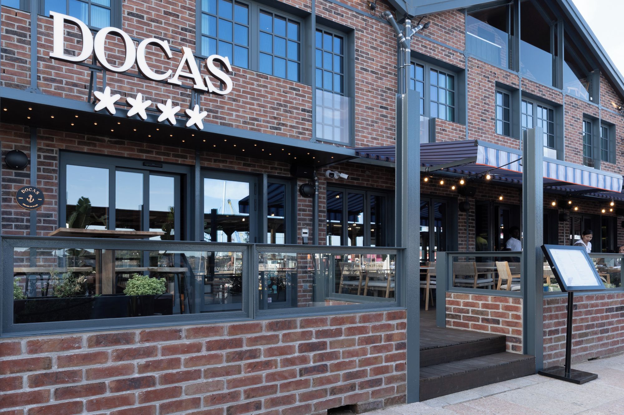 A brick building with a sign reading 'DOCAS' and outdoor seating.