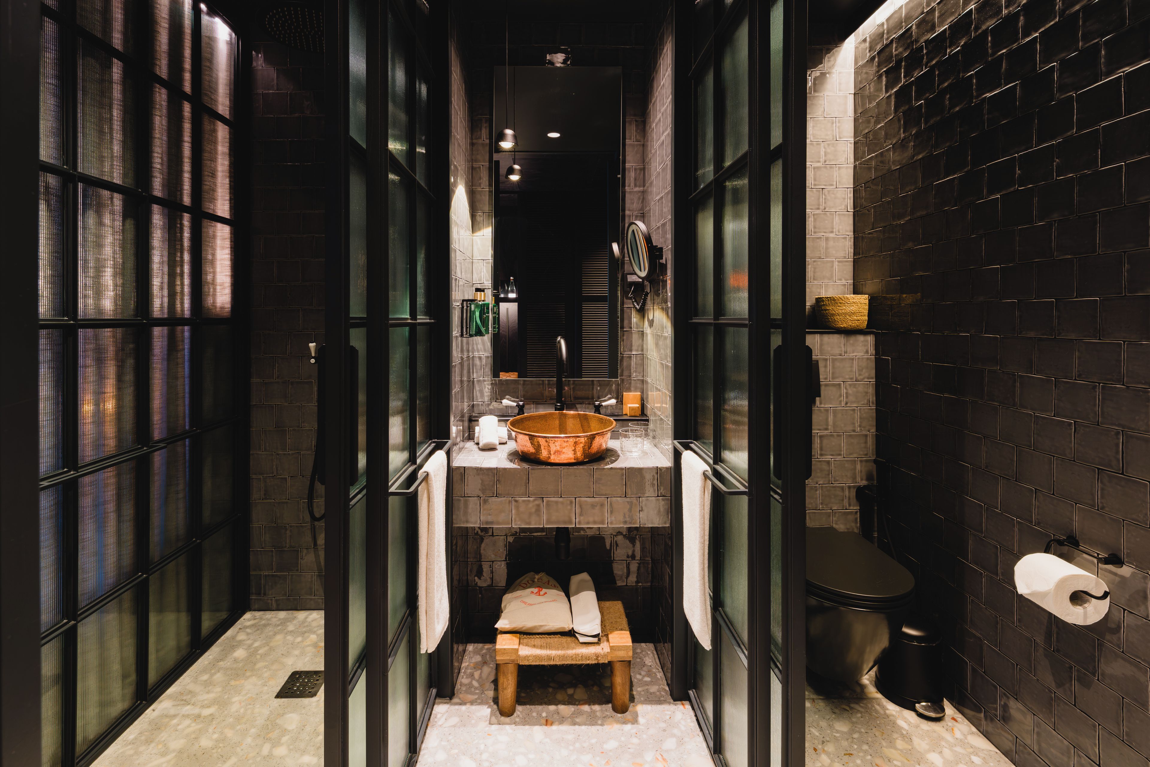 A narrow, dark hallway with a tiled wall and a bench with a towel.