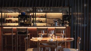 A bar area with a round table and chairs, a variety of bottles and glasses, and a tiled backsplash.