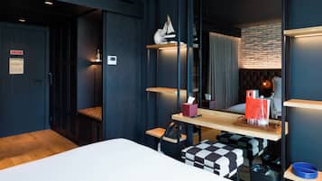 Quarto de hotel moderno com cama, escrivaninha, computador, telefone e espelho.