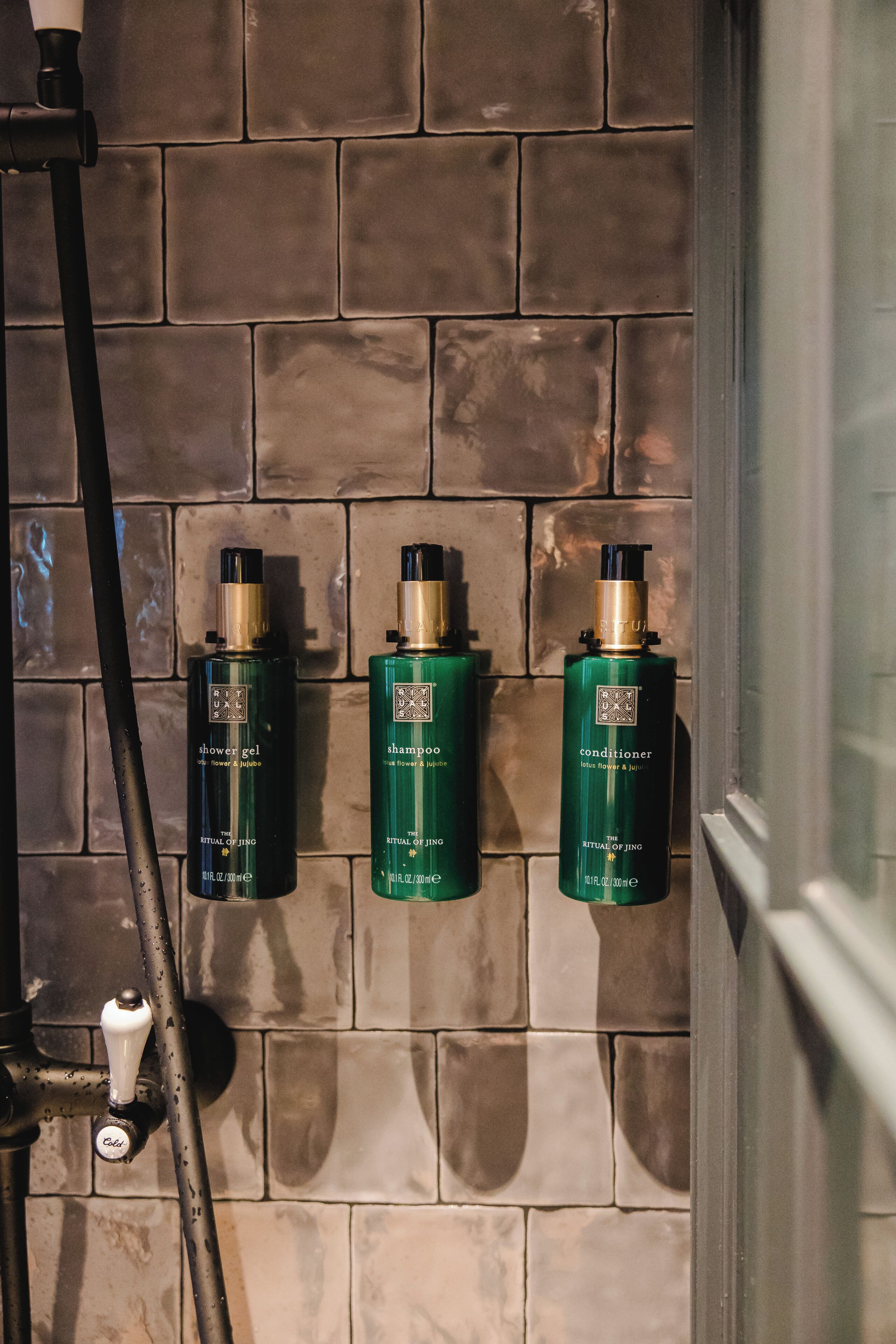 A bathroom with a tiled wall and three bottles of lotion.