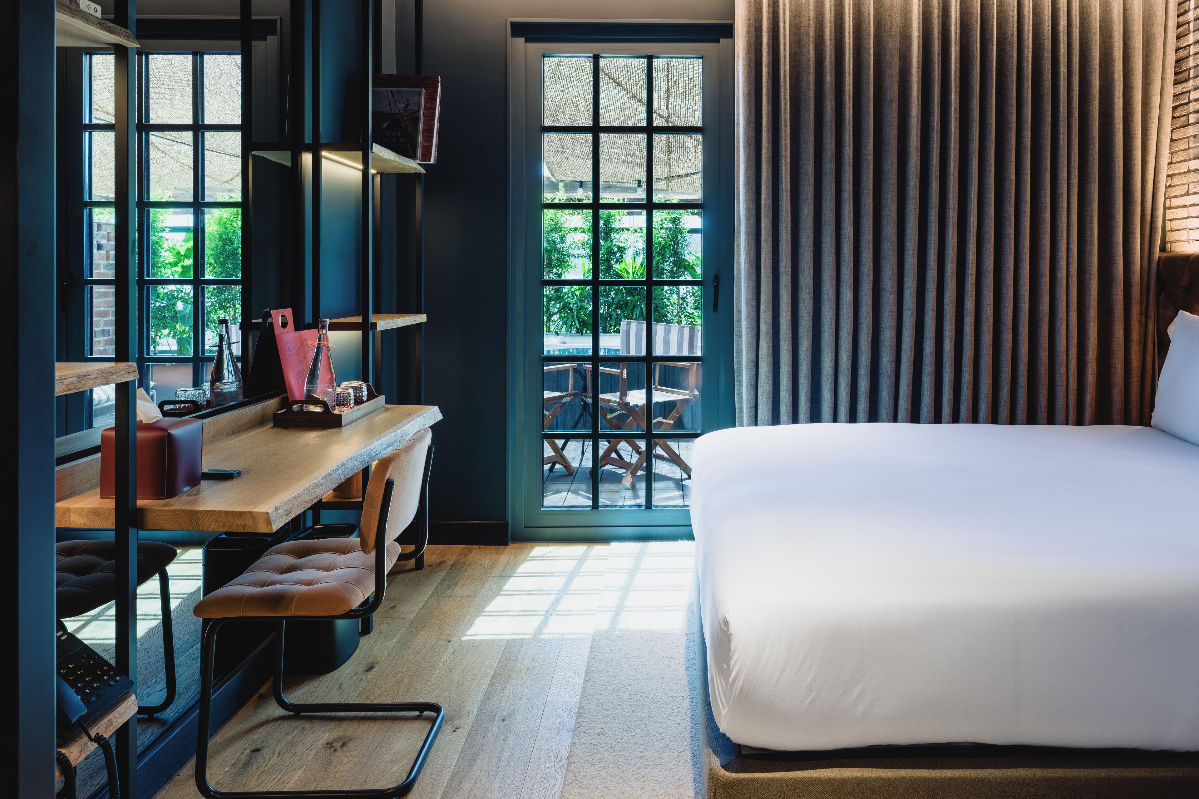 Habitación de hotel con una cama, un escritorio con computadora y una ventana que ofrece vistas a zonas verdes.