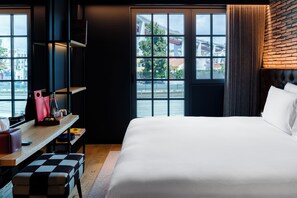 A hotel room with a large bed, a desk with a chair, and a view of the city through large windows. - Docas Hotel Lisbon (Lisbon)