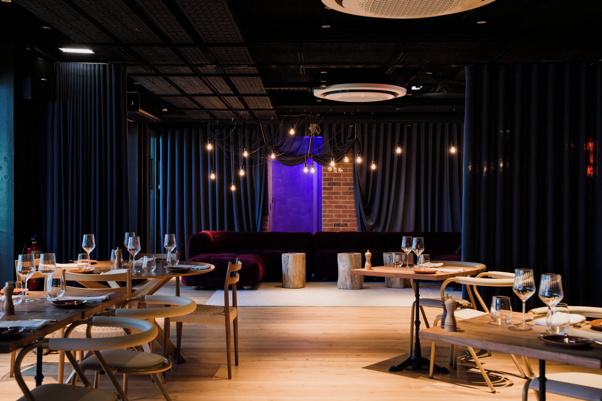Een restaurantinterieur met houten tafels, stoelen en een podium met gordijnen.