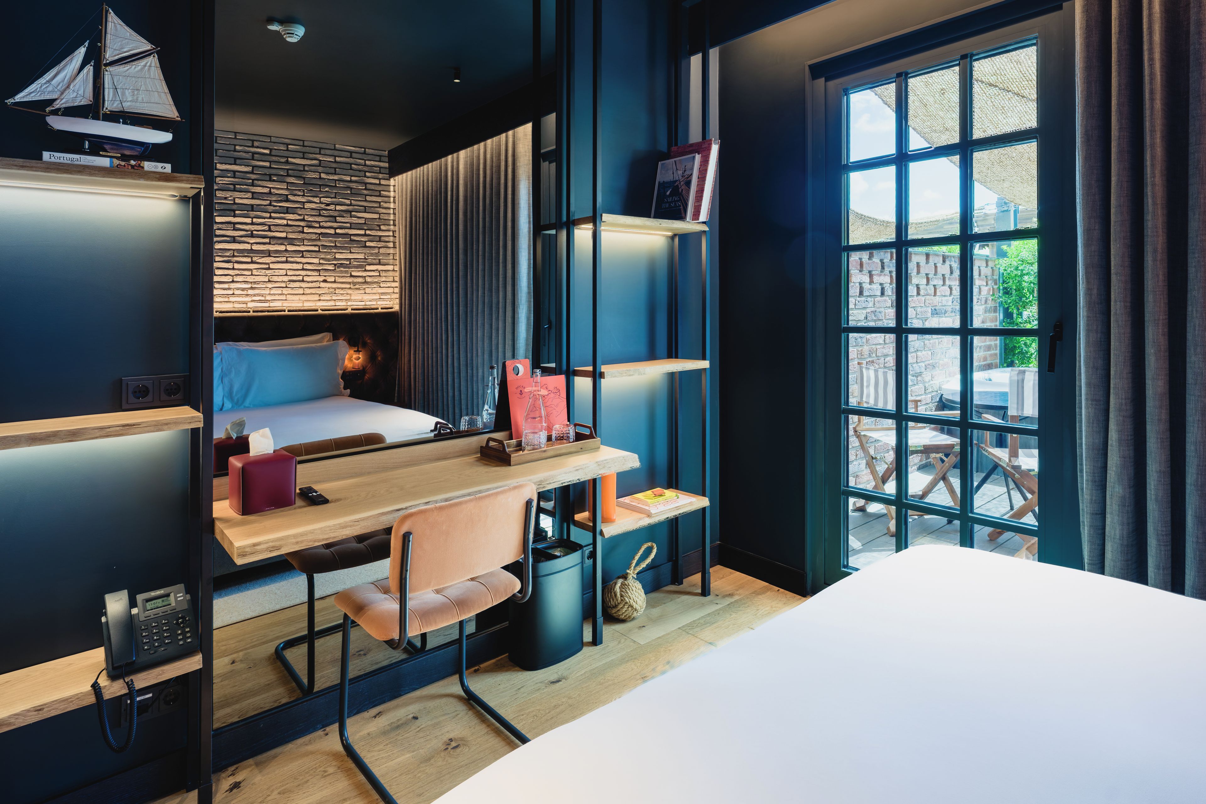 A modern room with a bunk bed, a desk with a chair, a bookshelf, and a window with a view of the outside.