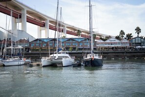 A marina with several boats docked, a bridge overhead, and buildings with outdoor seating in the background. - Docas Hotel Lisbon (Lisbon)